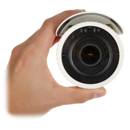 A hand holds a compact, white security camera with a prominent lens and a protective cover. The design is sleek and modern, suitable for discreet surveillance.