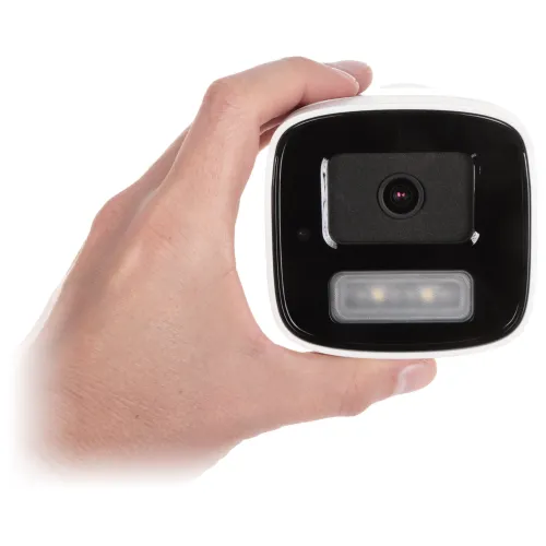 A person holds a compact, square-shaped security camera with a black front panel featuring a lens and LED lights. The camera is designed for easy installation and discreet surveillance.