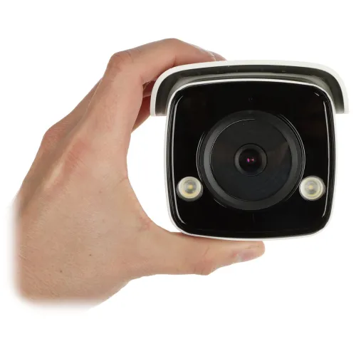 A hand is holding a compact, square-shaped security camera with a black front and two small LED lights. The camera features a prominent lens in the center, designed for surveillance purposes.