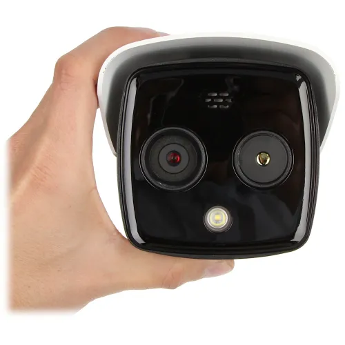 A person is holding a compact, dual-lens security camera with a sleek black front and a white casing. The camera features an LED light and is designed for surveillance purposes.