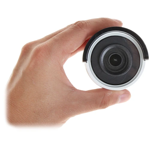 A hand is holding a compact, cylindrical security camera with a prominent lens. The camera features a sleek design with a black and silver finish.
