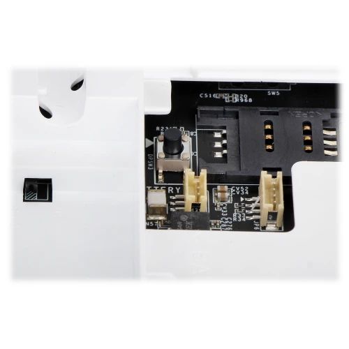 Close-up view of an electronic circuit board featuring various connectors and a small push button. The board is partially enclosed in a white plastic casing with visible slots and openings.