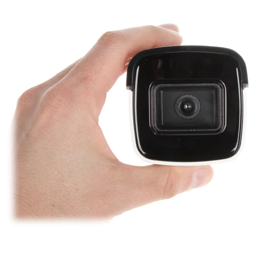 A hand is holding a compact, black security camera with a sleek, square design. The camera lens is prominently centered, surrounded by a glossy finish.