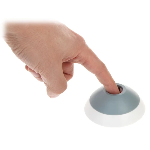 A hand is pressing a button on a small, dome-shaped device with a gray top and white base. The device appears to be designed for easy activation with a simple touch.