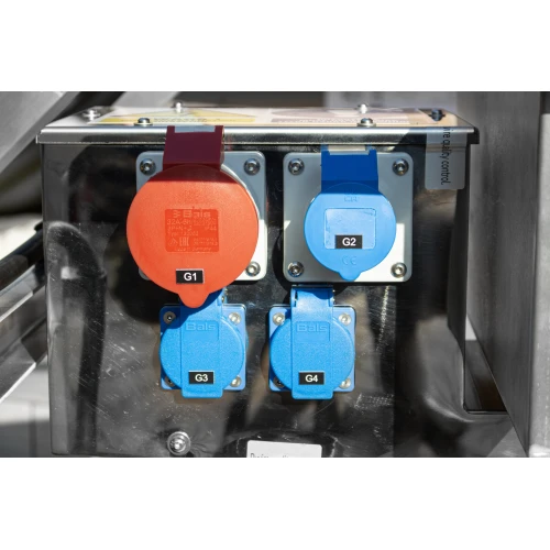 The image shows a close-up of a generator's power outlets, featuring two red and two blue sockets with protective covers. The metallic casing and clear labeling indicate a robust and organized design for efficient power distribution.