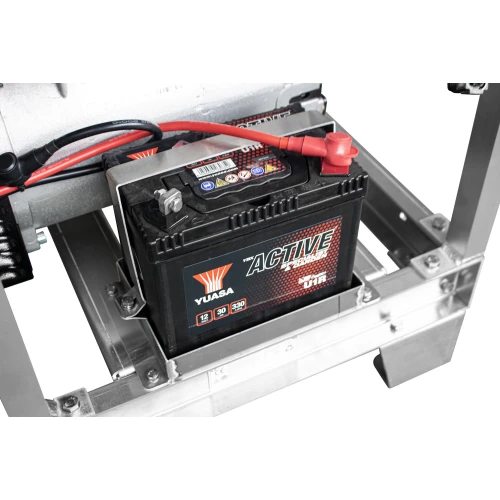 The image shows a Yuasa Active battery securely mounted within a metal frame, featuring red and black cables connected to its terminals. The battery is designed for reliable power supply, suitable for use in generators or other machinery.