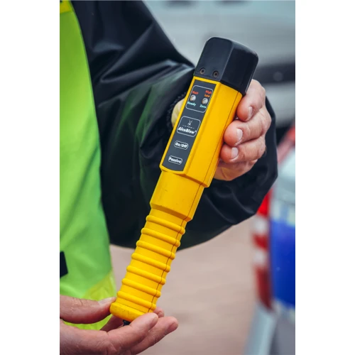 A person is holding a yellow handheld breathalyzer with a black top and several buttons on the front. The device is designed for quick and easy alcohol detection, featuring a ribbed grip for secure handling.