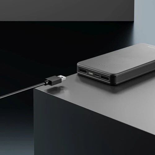 A sleek black power bank with multiple USB ports is shown on a minimalist dark surface. A USB cable is connected to one of the ports, highlighting its charging capability.