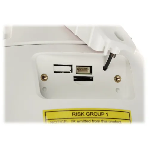 The image shows a close-up of a device featuring a memory card slot and a reset button. The panel is white with a yellow warning label indicating "Risk Group 1" for infrared emissions.