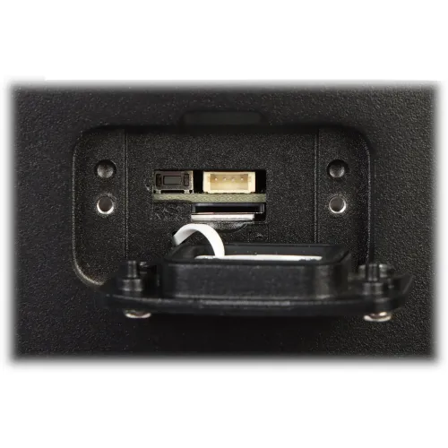 The image shows a close-up of a memory card slot and a reset button on a black electronic device. The compartment is open, revealing connectors and a white cable inside.