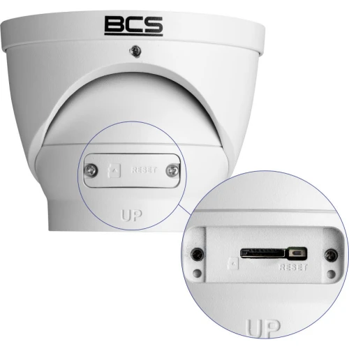 A white dome-shaped IP camera with a BCS logo, featuring a durable housing suitable for outdoor use. The close-up inset highlights the reset button and connection port for easy access and maintenance.