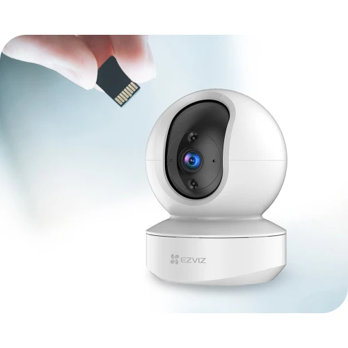 A sleek, white, spherical security camera with a rotating lens is shown alongside a hand holding a microSD card for storage expansion. The camera features a modern design and is suitable for indoor surveillance.
