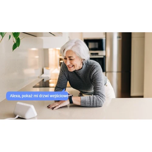A woman interacts with a smart home device on a kitchen counter, displaying a voice command feature. The device is compact and designed for seamless integration into modern home environments.