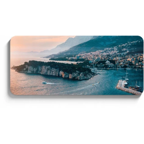 A scenic coastal landscape featuring a rugged peninsula surrounded by calm blue waters, with a small boat navigating near the shore. The background showcases a picturesque town nestled at the base of majestic mountains under a soft, pastel sky.
