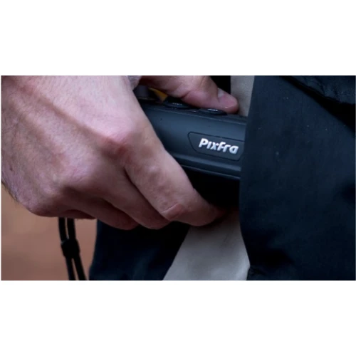 A person is holding a Pixfra thermal imaging monocular, partially concealed by a dark jacket. The device is compact and designed for easy handling and portability.