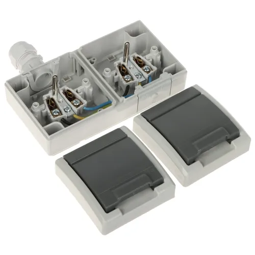 The image shows a gray electrical junction box with two compartments, each containing wiring terminals and a cable gland. Two detachable covers are placed in front, designed to protect the internal components.