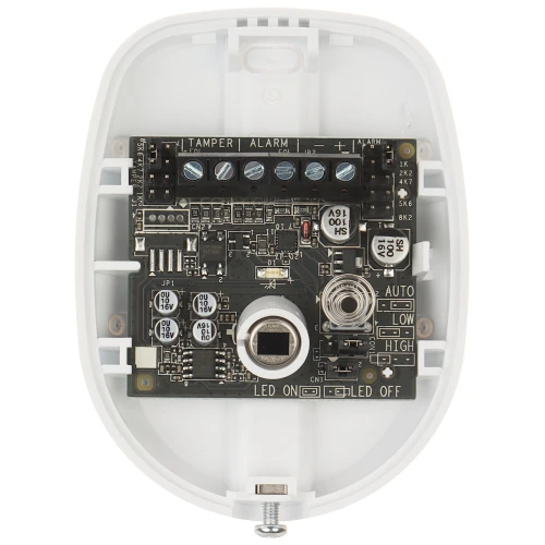 The image shows the interior of a white electronic device featuring a circuit board with various components, including capacitors, resistors, and connectors. The device is designed for security purposes, with labeled sections for tamper and alarm functions.