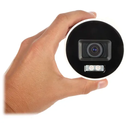 A hand holds a compact, round security camera with a prominent lens and two small LED lights beneath it. The camera features a sleek black and white design, suitable for discreet surveillance.