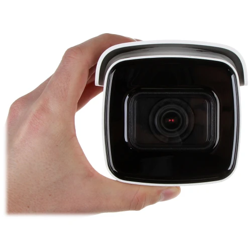 A person is holding a compact, square-shaped security camera with a black front and a white casing. The camera lens is prominently centered, surrounded by a glossy black surface.